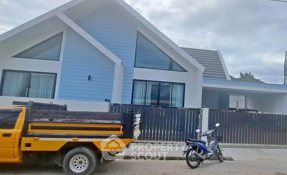Modern blue and white house with large windows and sloped roof, featuring a fenced yard.
