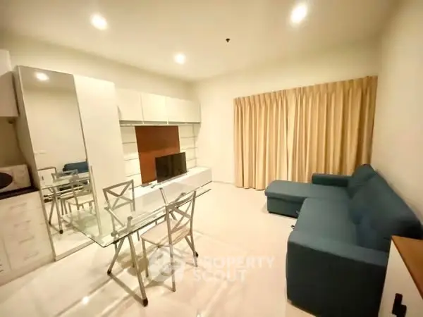 Modern living room with glass dining table and blue sofa in cozy apartment.