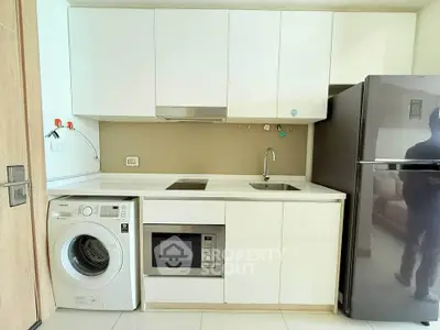 Modern kitchen with sleek white cabinets, built-in appliances, and washing machine in compact layout.