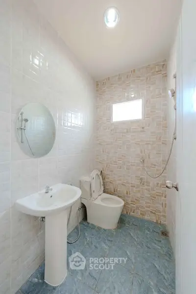 Modern bathroom with sleek fixtures and tiled walls, featuring a pedestal sink and shower.
