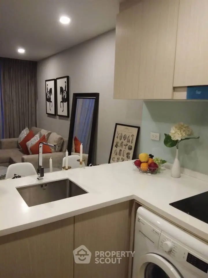 Modern kitchen with sleek design, integrated washing machine, and cozy living area in open layout apartment.