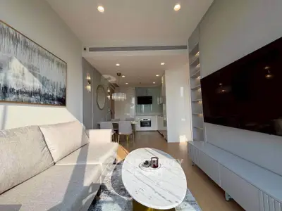 Modern living room with open kitchen, featuring sleek furniture and large wall-mounted TV.