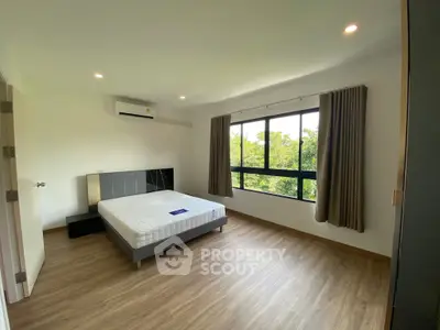 Spacious bedroom with large window and modern decor in a serene setting.