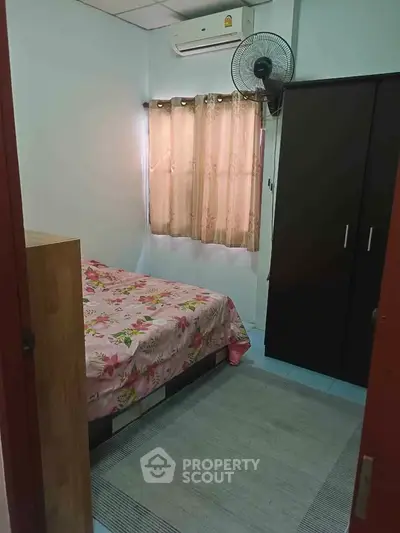 Cozy bedroom with floral bedding and dark wardrobe, featuring air conditioning and natural light.
