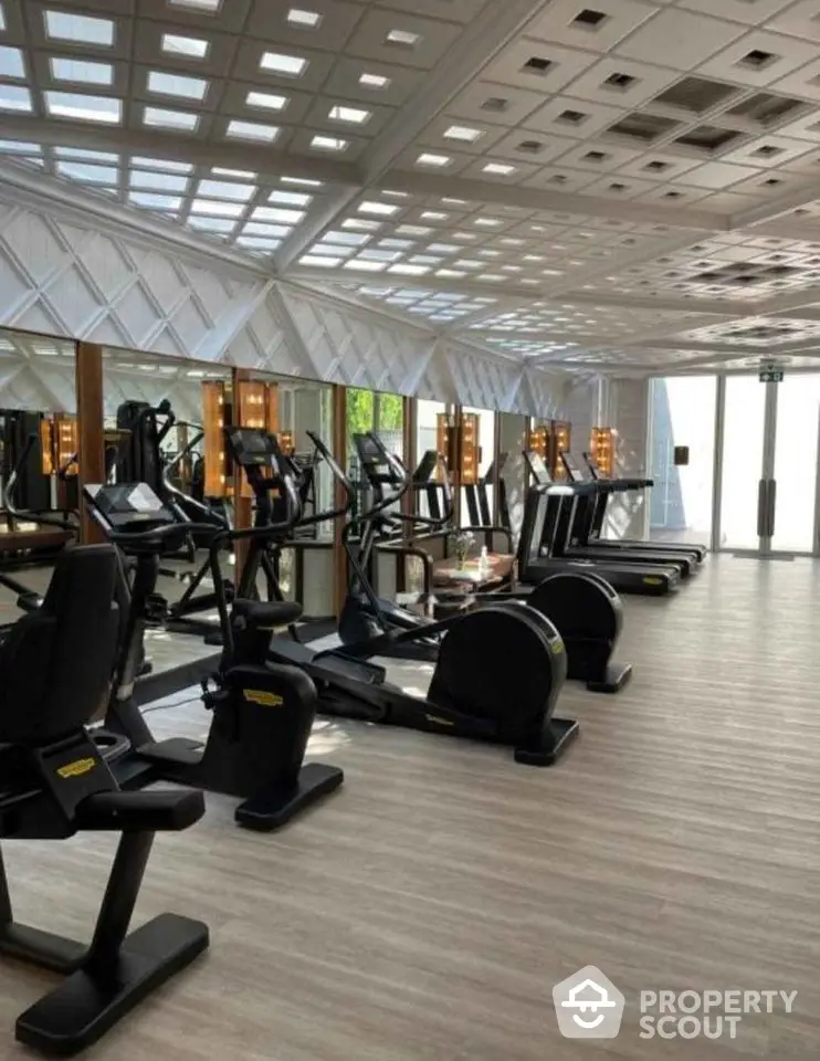 Luxurious gym with modern equipment and ample natural light in upscale residential complex.