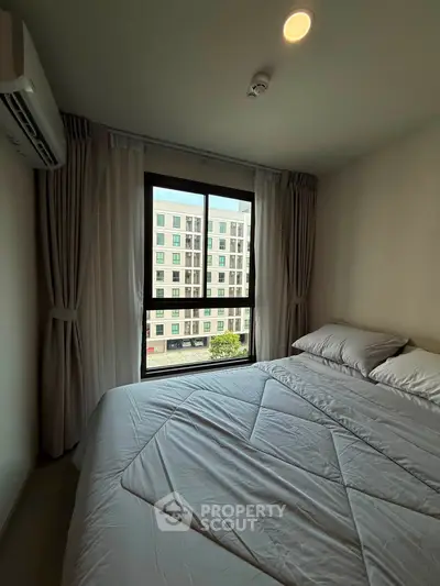 Cozy bedroom with large window offering city view, featuring a comfortable bed and elegant curtains.