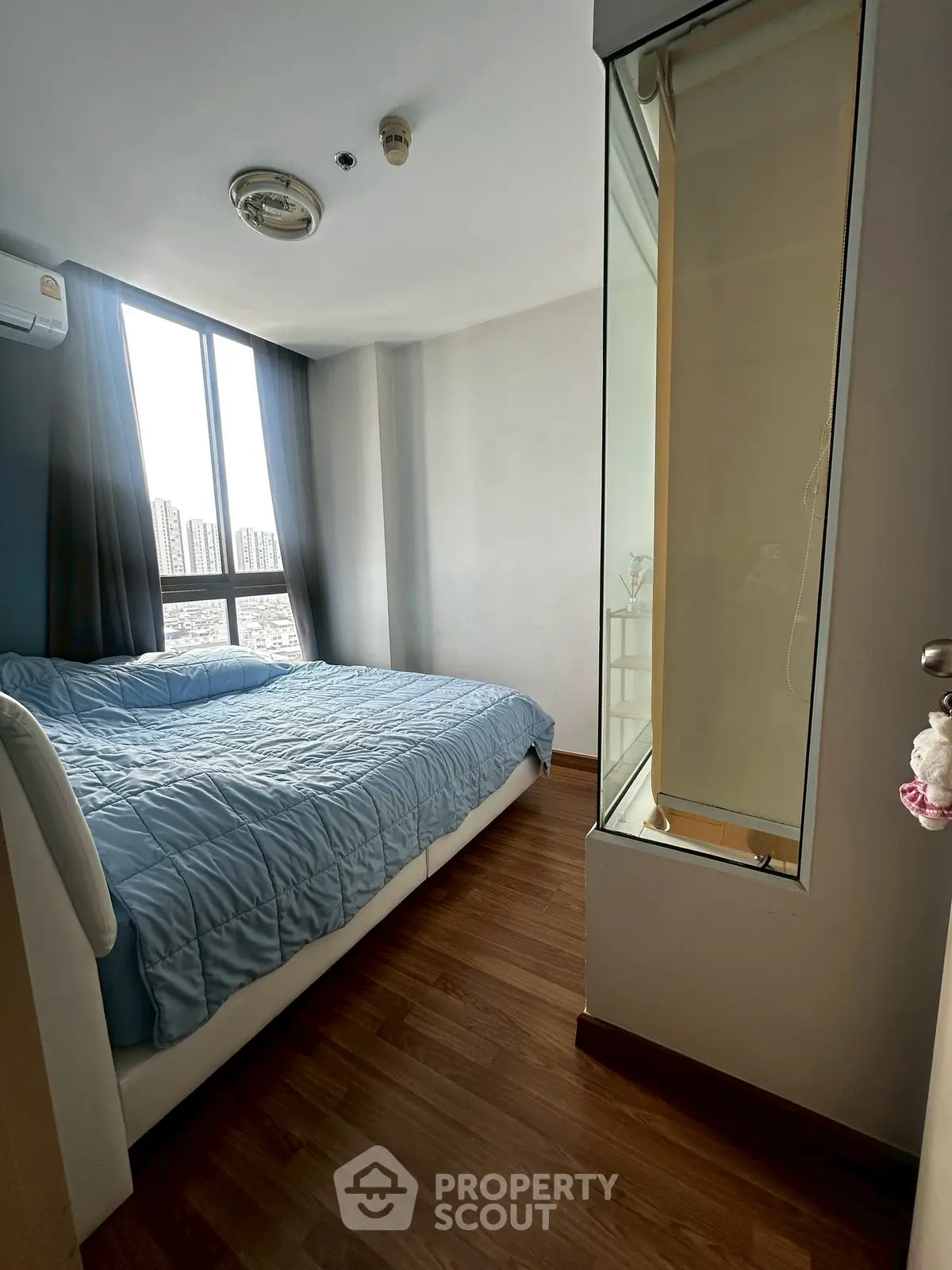 Cozy bedroom with large window offering city views, featuring a comfortable bed and wooden flooring.