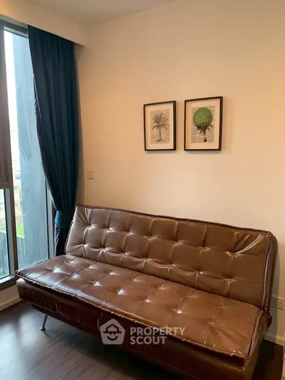 Stylish living room with leather sofa and framed art, featuring large window and elegant curtains.