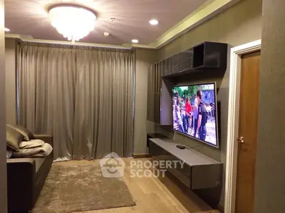 Modern living room with elegant chandelier and wall-mounted TV, featuring cozy seating and stylish decor.