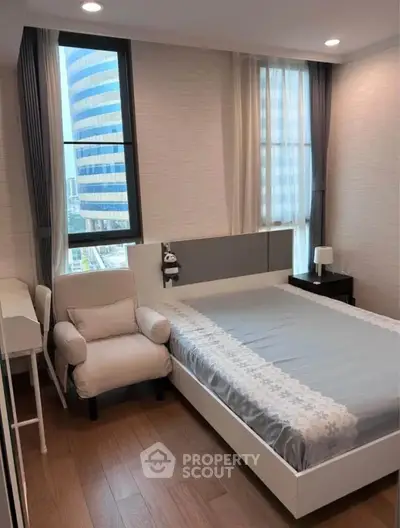 Modern bedroom with large windows and stylish furnishings in urban apartment.