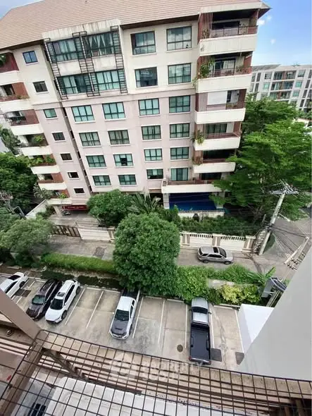 Stunning aerial view of modern apartment building with lush greenery and ample parking space.