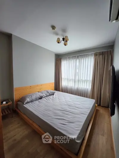 Cozy bedroom with wooden flooring and modern decor, featuring a large window for natural light.