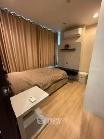 Cozy bedroom with modern decor and wooden flooring, featuring an air conditioner and stylish curtains.