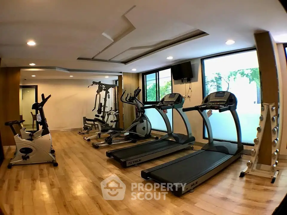Modern gym with state-of-the-art equipment and large windows in a residential building.
