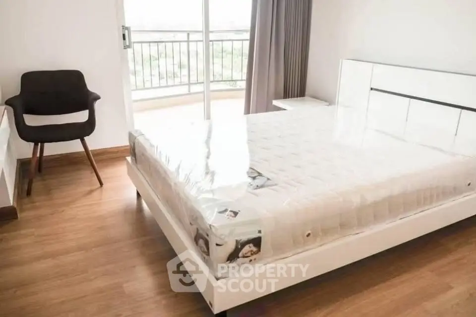Modern bedroom with sleek white bed and balcony view, featuring wooden flooring and stylish chair.