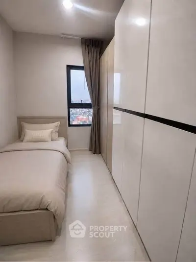 Cozy bedroom with single bed and large wardrobe, offering a serene city view through the window.