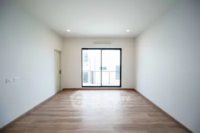 Spacious empty room with wooden flooring and large window in modern apartment.