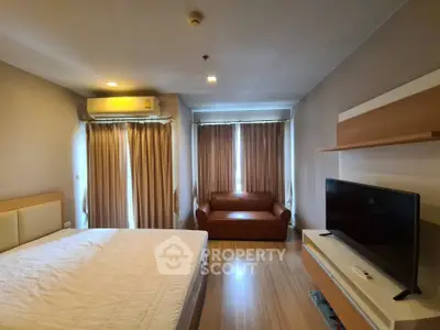 Spacious bedroom with modern decor and natural light, featuring a cozy sofa and flat-screen TV.