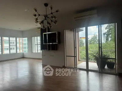 Spacious living room with modern chandelier and large windows offering natural light and balcony access.