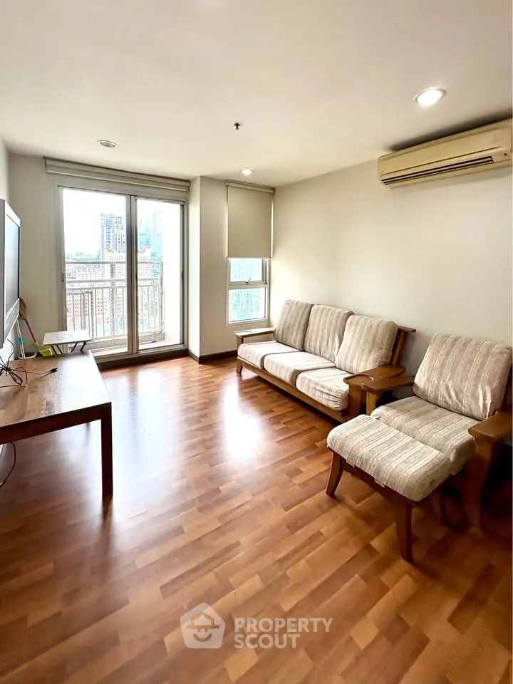 Spacious living room with wooden flooring and large windows offering city views.