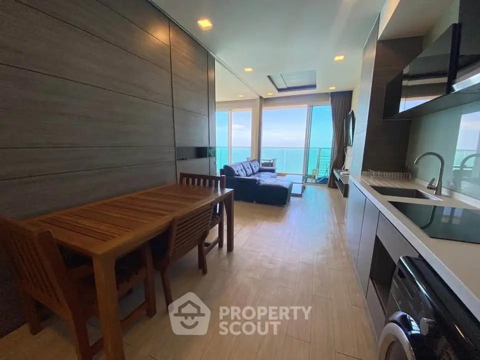 Modern open-plan living room with ocean view, sleek kitchen, and cozy dining area in luxury apartment.