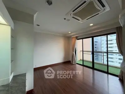 Spacious living room with balcony and city view, featuring wooden flooring and modern ceiling design.