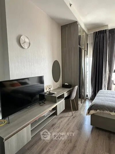 Modern bedroom with sleek furniture and natural light, featuring a TV and workspace.