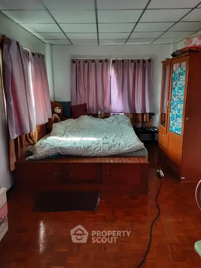 Cozy bedroom with wooden flooring and large windows with curtains