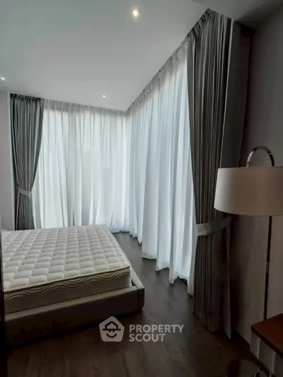 Spacious bedroom with floor-to-ceiling windows and elegant curtains, offering abundant natural light.