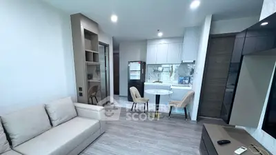 Modern open-plan living room with kitchen, featuring sleek design and cozy seating area.