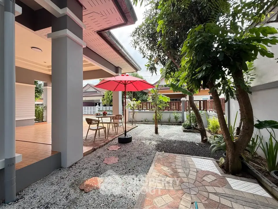 Charming garden patio with red umbrella and outdoor seating, perfect for relaxation.