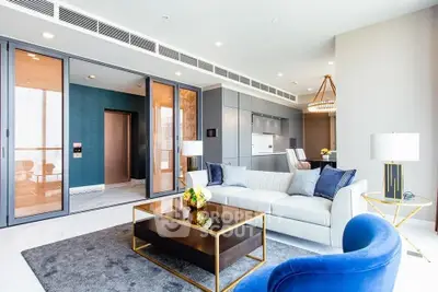 Luxurious modern living room with plush seating and open-plan kitchen, leading to a sunlit balcony with a view.