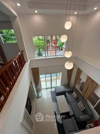 Spacious living room with high ceiling and modern decor, featuring large windows and elegant lighting.