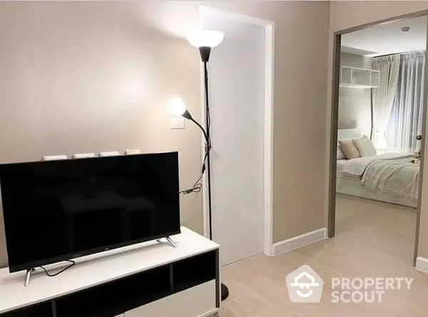 Modern minimalist living room with sleek TV console and ambient lighting, leading to a cozy bedroom with mirrored closet doors.