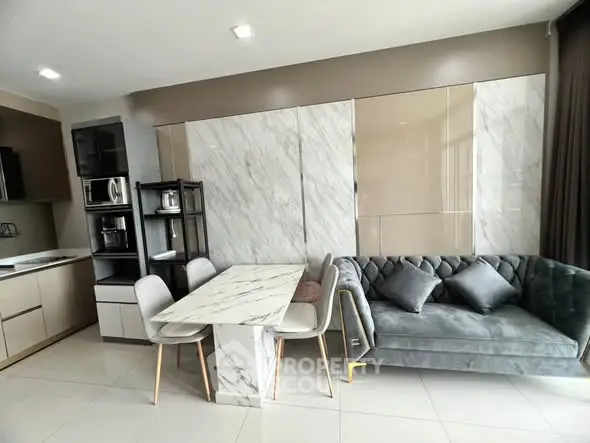 Modern open-layout kitchen and living room with marble dining table and plush gray sofa.
