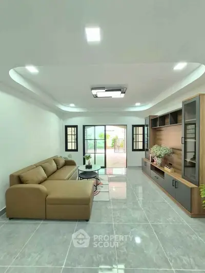 Spacious modern living room with elegant sofa and entertainment unit, featuring large windows and glossy tiled floor.