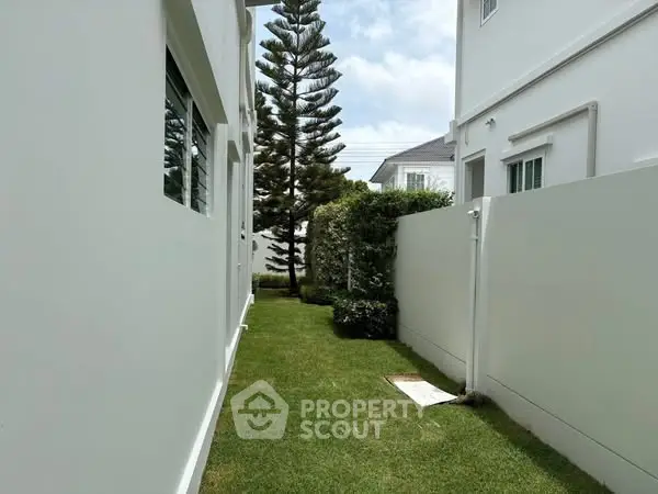 Modern exterior view of a white house with lush green lawn and privacy fence.