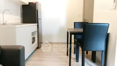 Modern compact kitchen with dining area and sleek black chairs in a cozy apartment.