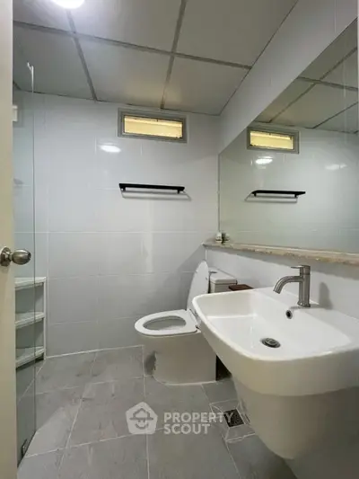 Modern bathroom with sleek fixtures and neutral tiles, featuring a spacious sink and toilet.