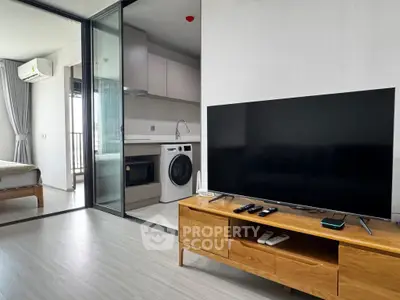 Modern living room with TV, wooden furniture, and view into kitchen and bedroom.