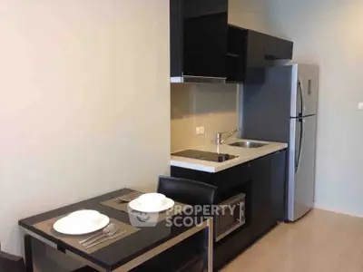 Modern compact kitchen with sleek black cabinets and dining area in stylish apartment.