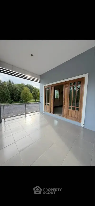 Spacious balcony with sliding wooden doors and scenic view of lush greenery.