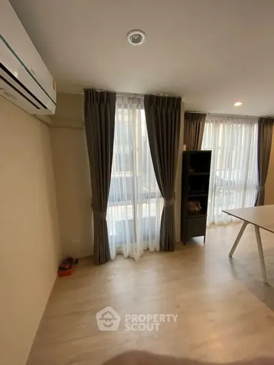 Spacious living room with large windows and elegant curtains, featuring modern air conditioning unit.