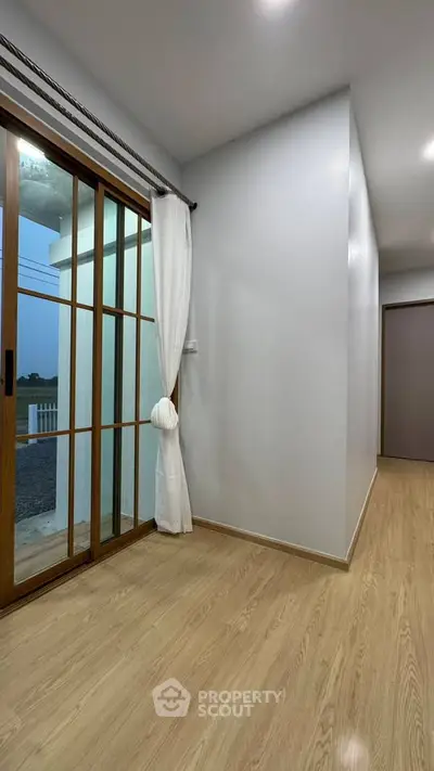Modern hallway with wooden flooring and sliding glass door leading to balcony.