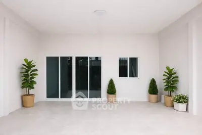 Spacious minimalist balcony with sliding glass doors and potted plants, perfect for relaxation.