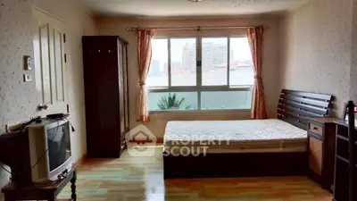 Spacious bedroom with large window and city view, featuring wooden furniture and cozy ambiance.