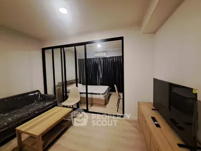 Modern living room with glass partition to bedroom, featuring sleek furniture and ambient lighting.