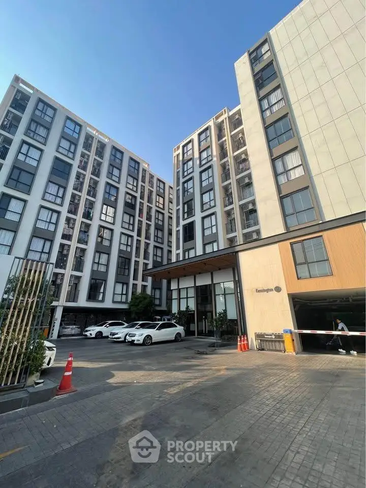 Modern apartment building exterior with parking area and clear blue sky.