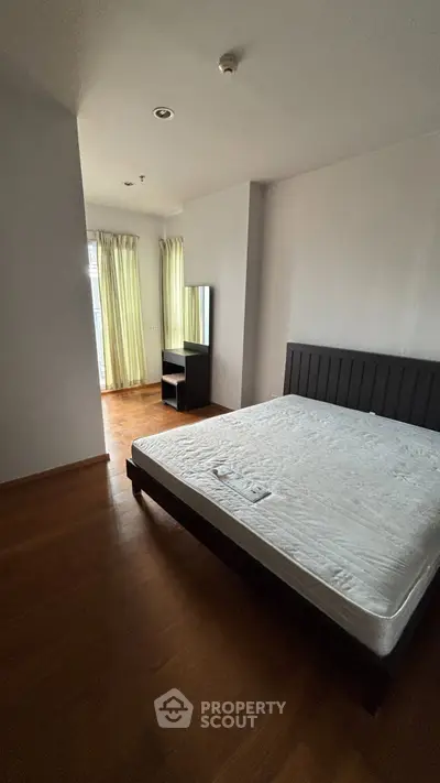 Spacious bedroom with large windows and hardwood floors in modern apartment.