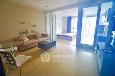 Modern open-plan living room with glass partition and cozy bedroom view.